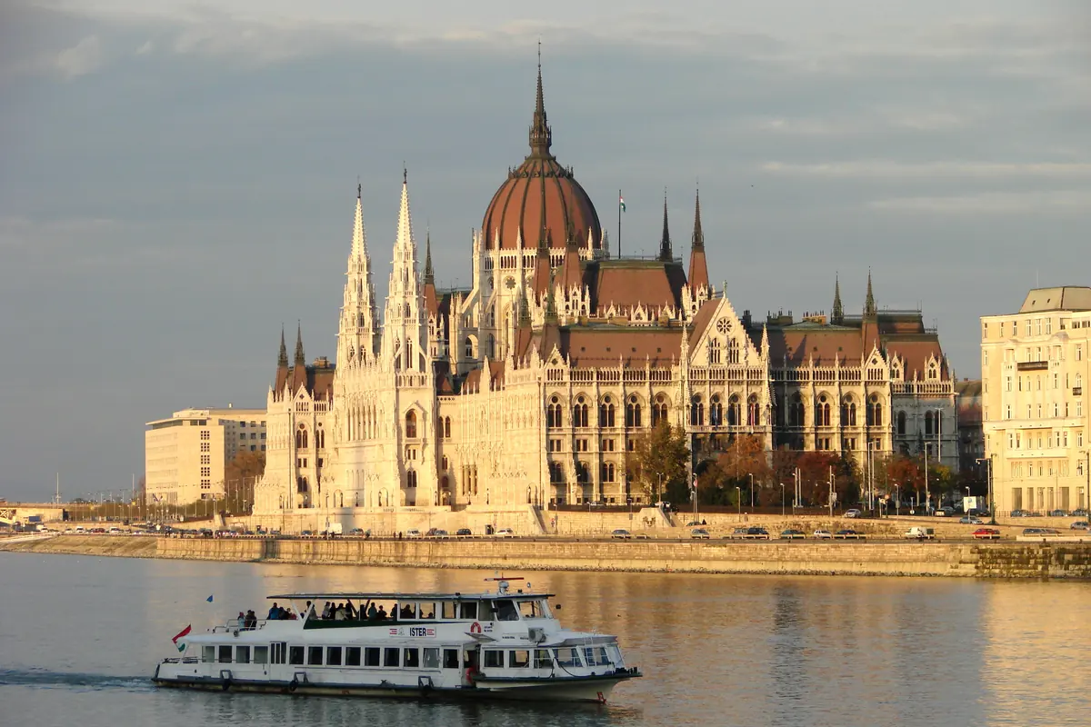 A passenger boat on the Danube in front of the neo-Gothic Hungarian Parliament Building on the Pest bank, lit by low evening sun