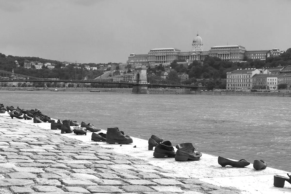 Black and white view along the Pest embankment, with iron shoes at the water's edge and the Chain Bridge and Buda Castle across the river