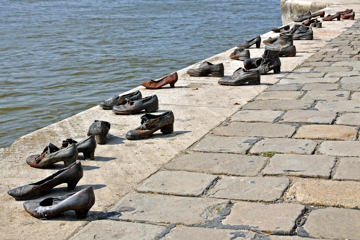 A row of rusted iron shoes, men's, women's and children's, set into the stone edge of the Danube embankment beside cobblestones